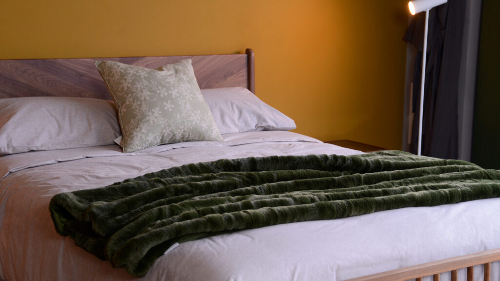 soft and luxurious faux fur throw in olive green shown dried on a bed