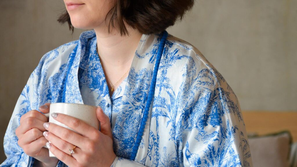 model holding a mug, wearing white PJs with blue jungle print. Pompom detailing around collar.