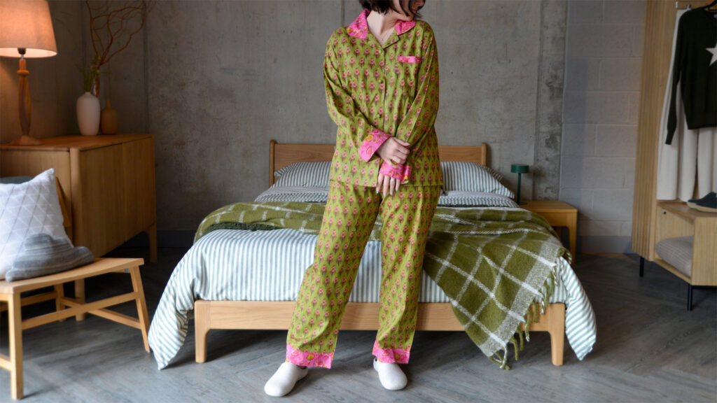 Model wearing green and pink PJ set with flora pattern stood in front of an oak bed and furniture.