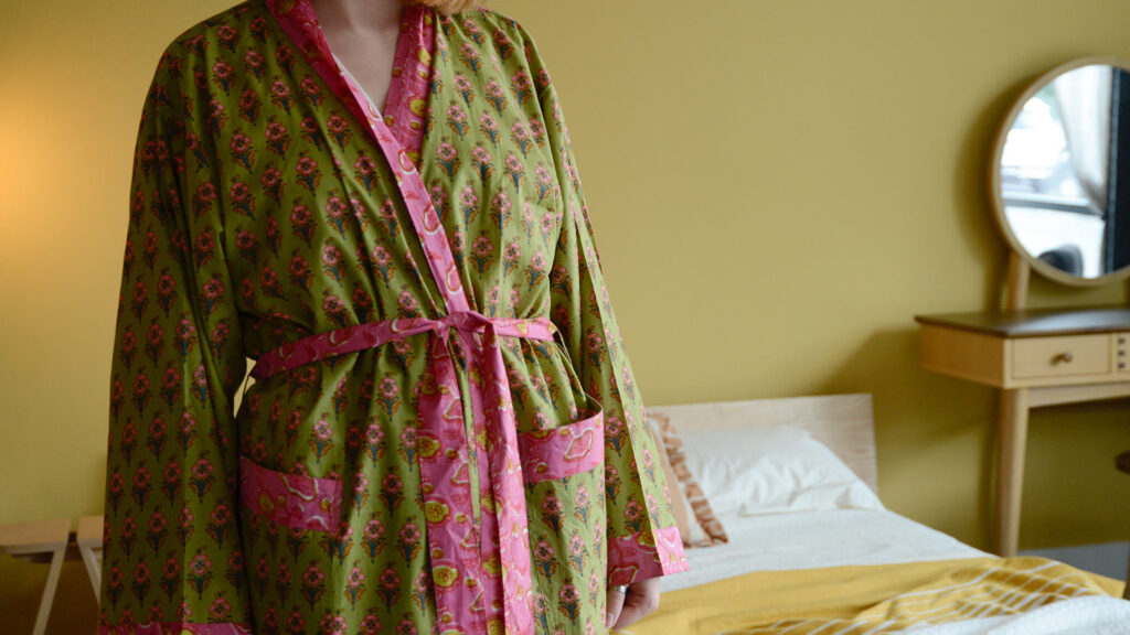 Image showing a green and pink floral robe on model. Shows detail of the green background of the robe, overlaid with a pink floral pattern and bright pink trim.