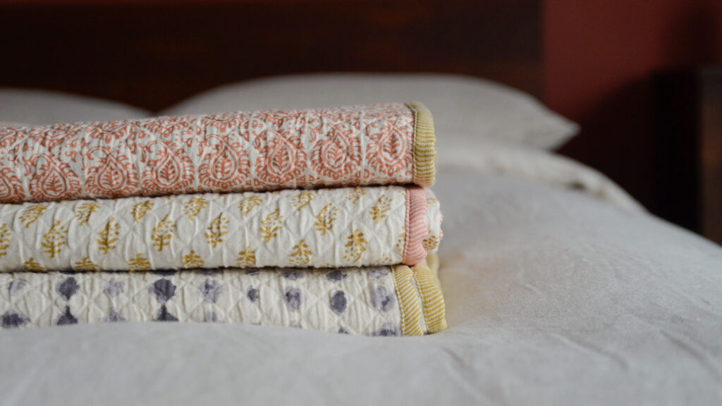 Stack of three contrast edged boho throws, one with ink blot pattern, one mustard diamonds and one terracotta tiles.