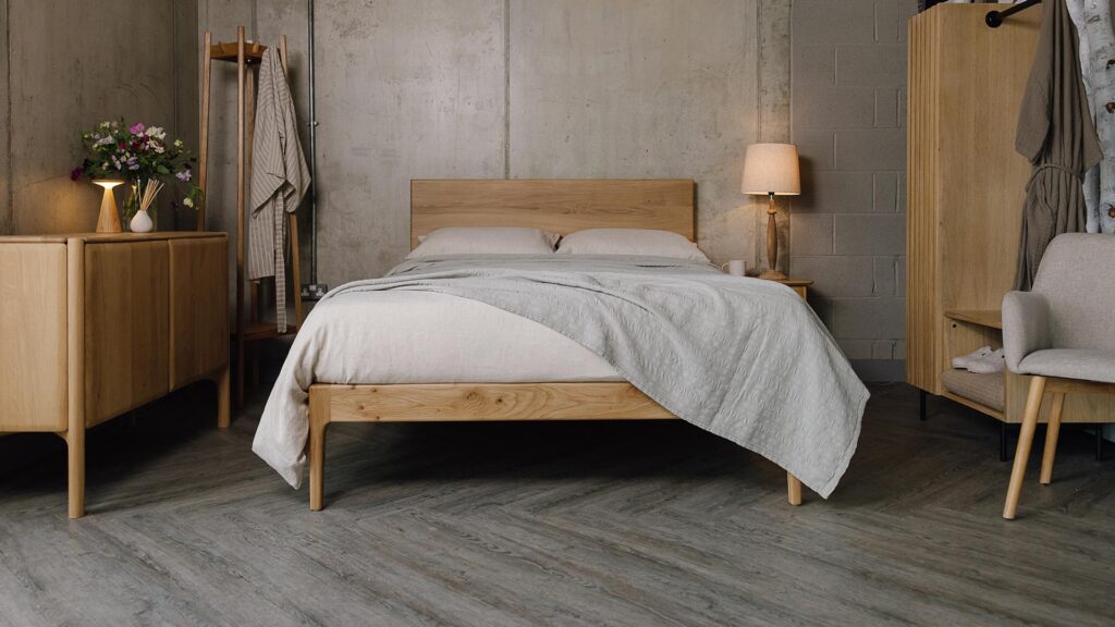A forward facing shot of the English oak Chiswick, dressed in the organic linen bedding in ecru. The bedding is mostly covered up by a embroidered striped bedspread in the colour silver-grey, which also overhangs the bottom right-hand corner of the bed base.