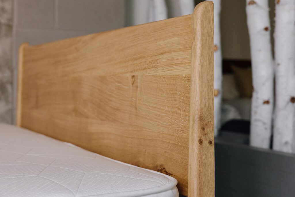 side view of Camden headboard, focus on headboard legs. Knots and cats paws visible in the English oak.