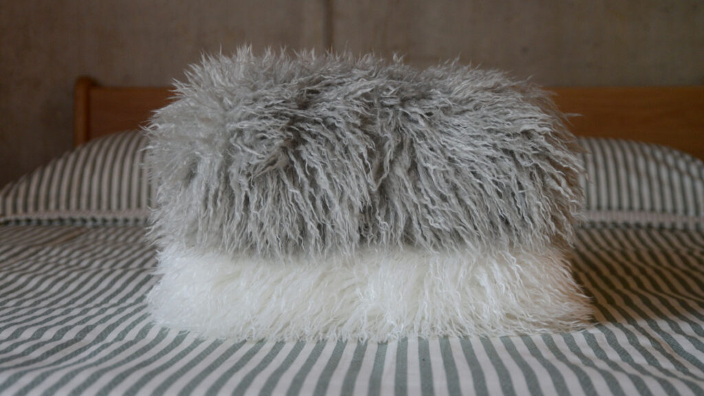 Image showing a stack of two faux afghan throws. The top is in a soft grey colour, and the bottom is in a pure white.