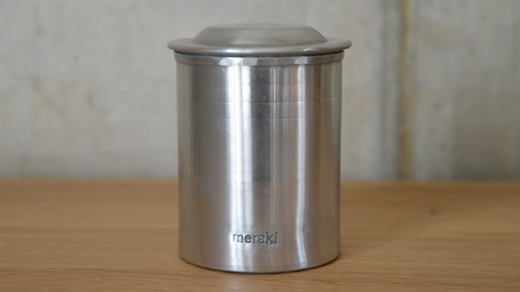 close up of silver storage jar with lid and meraki logo.