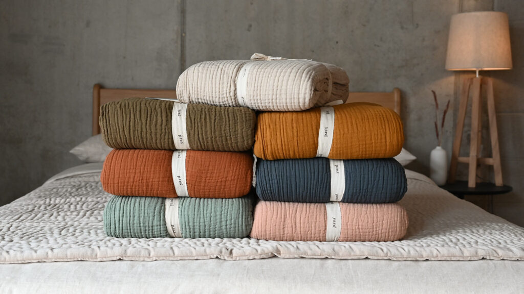 Muslin bedspreads in various colours, neatly folded and stacked.
