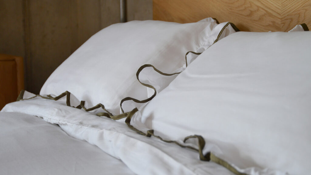 close up of pure white pillow with olive green edge and ruffled trim.