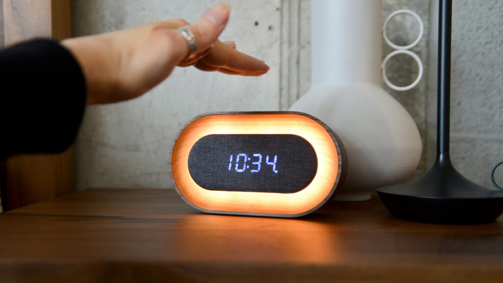 Walnut alarm clock with digital display panel. Hand photographed about to tap the top to adjust the light.