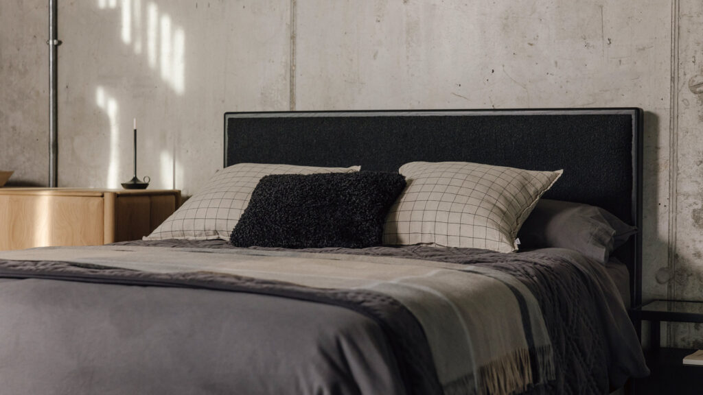 black oak upholstered bed with dark grey linen, a neutral throw and ecru and black check cushions.