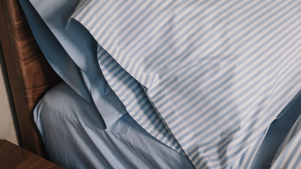 Blue and white striped cotton duvet cover and pillowcase set shown with pale blue chambray bedding