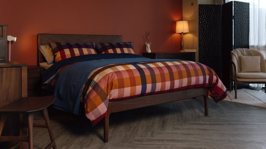 cosy bedroom scene with smoked walnut bed dressed in a bold check print bedding, topped with a neat deep blue bedspread.