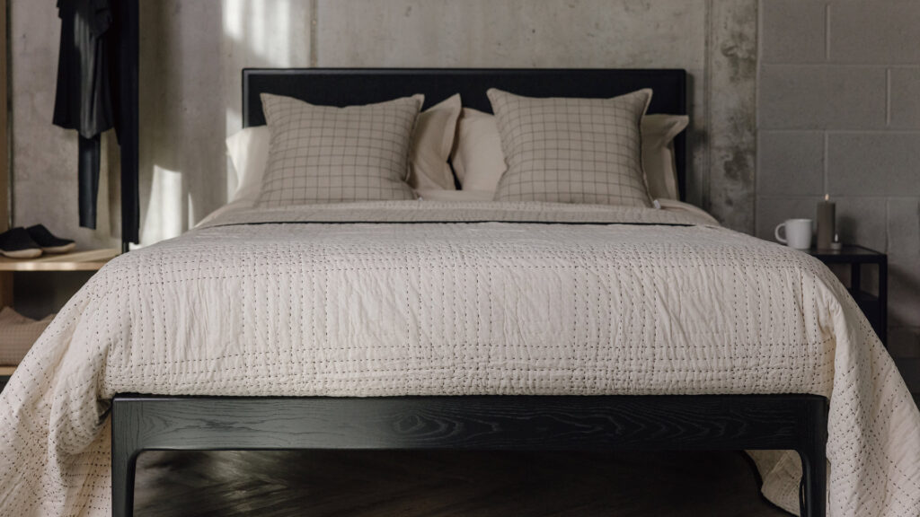 black oak bed frame with ecru quilt with black embroidered check pattern. Black check pillows also on bed.