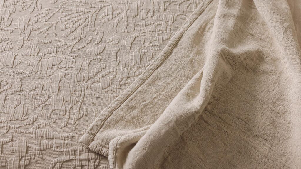Close up shot of the floral textured bedspread in the the ecru colour-way.