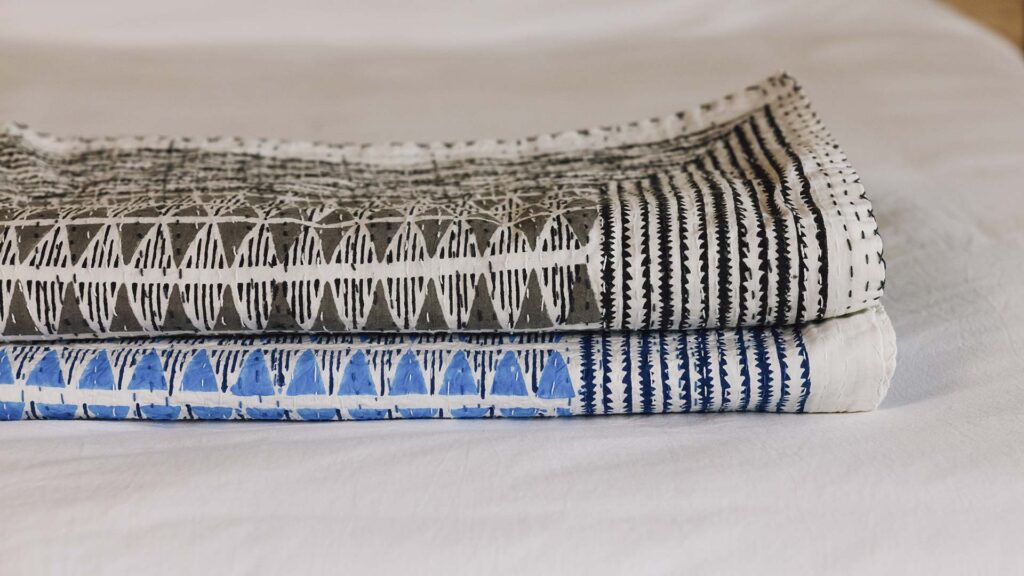 close up of grey and blue block print bedspreads, neatly folded on a white duvet.