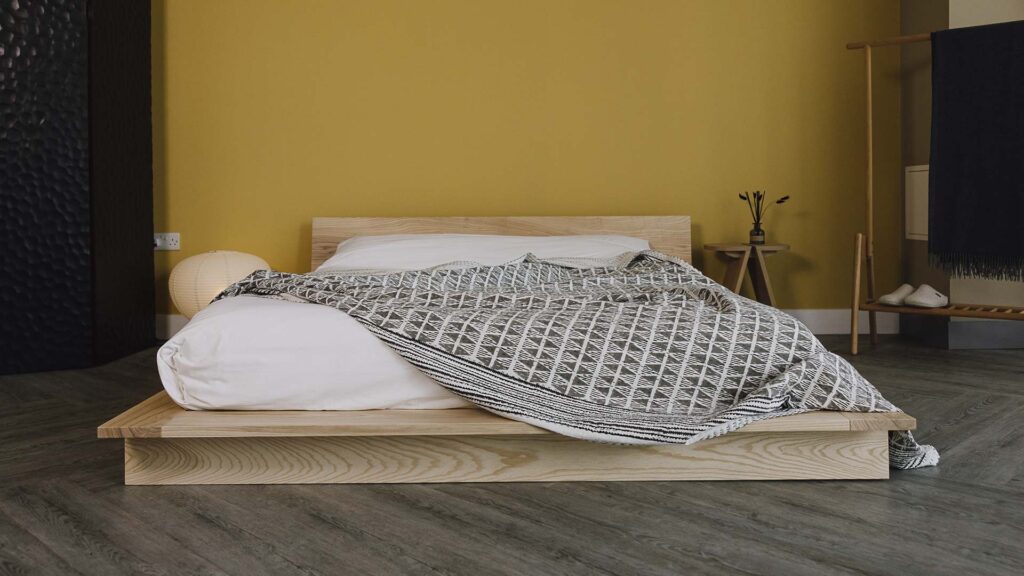 Oregon bed frame in solid ash with white bedding and a bedspread with a grey triangle block print.