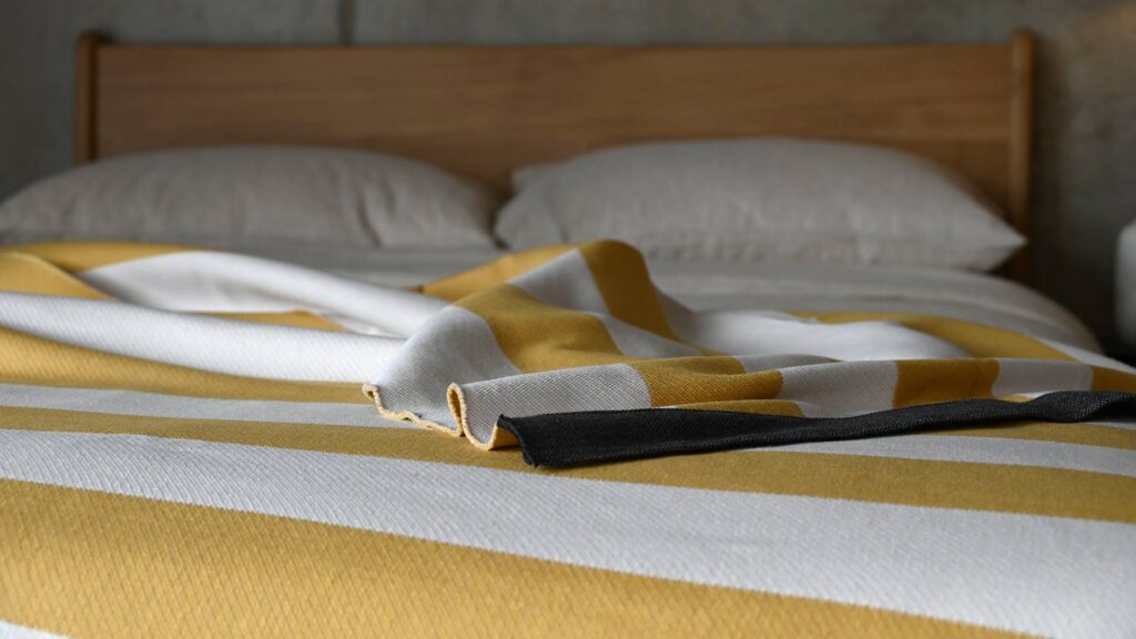 Closeup of an ivory and mustard striped throw laid on the top of a bed.
