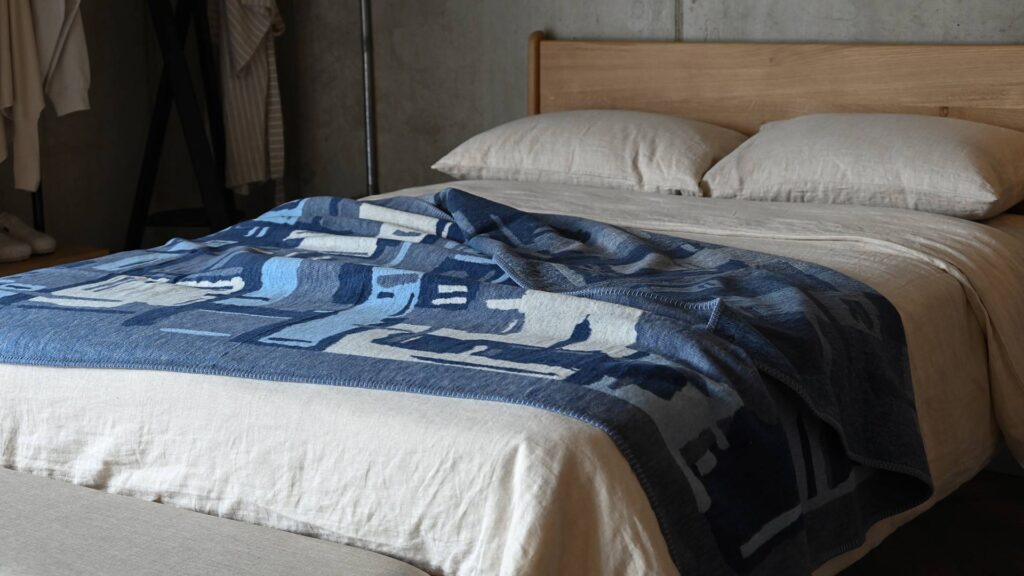 blue abstracted patterned throw laid out over stone bed linen on an oak bed.