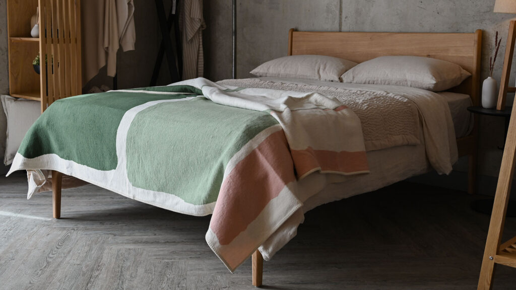 Throw with dark green, light green and pink colour blocks draped across a bed with stone linen.