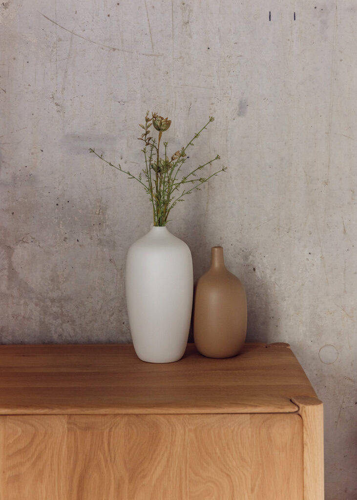 oak sideboard with 2 ceramic vases, one white and one stone.