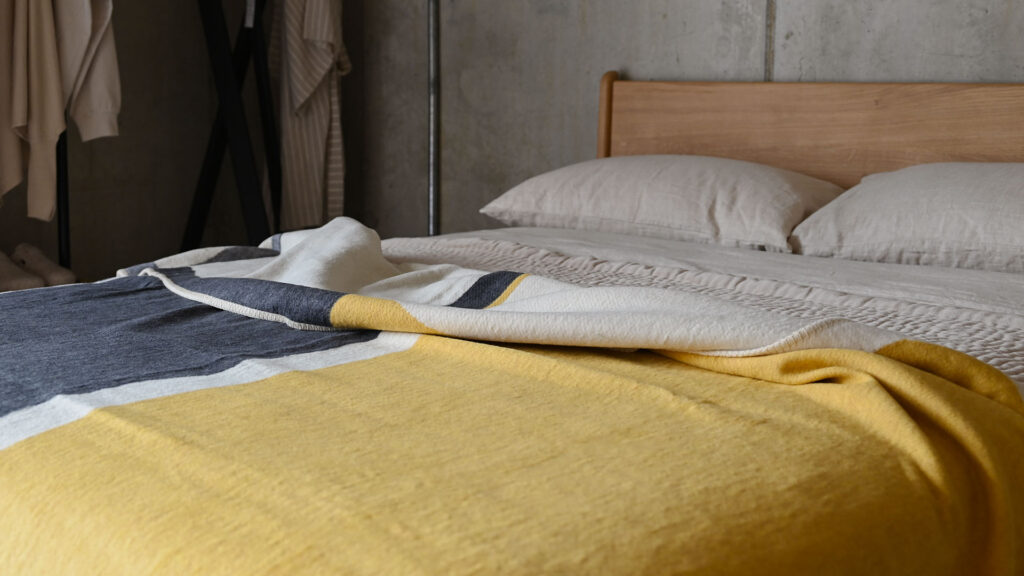 Yellow and grey block coloured throw draped across a bed dressed in stone linen.
