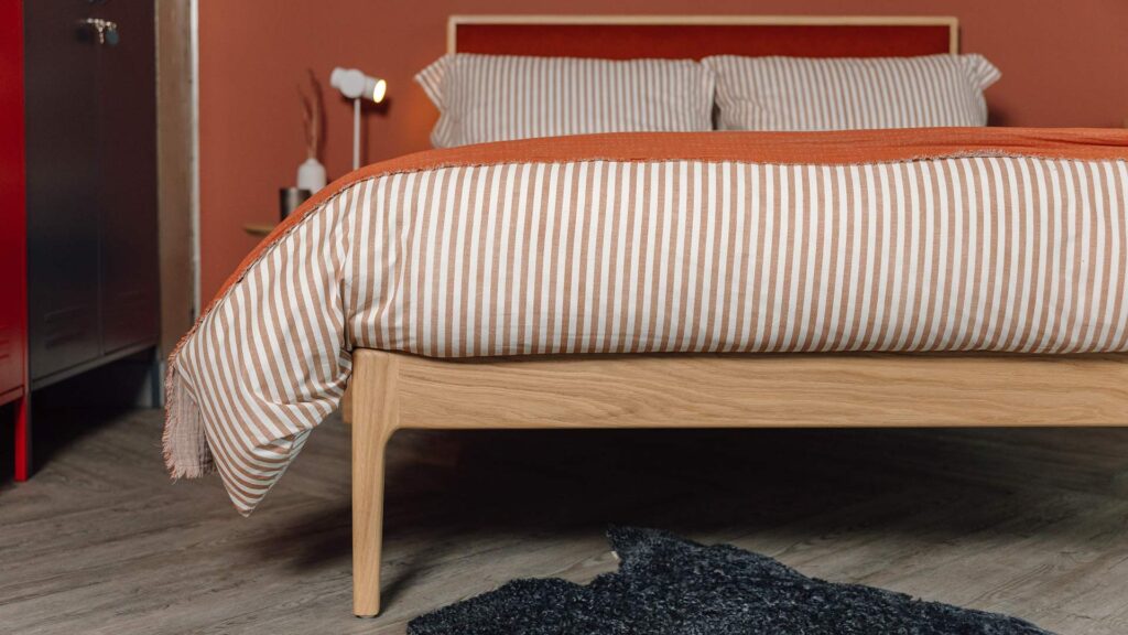 oak Carlisle bed leg detail with striped bedding in rust red