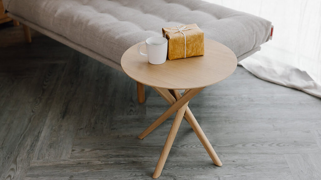 Oak round side table with gift and mug on top.