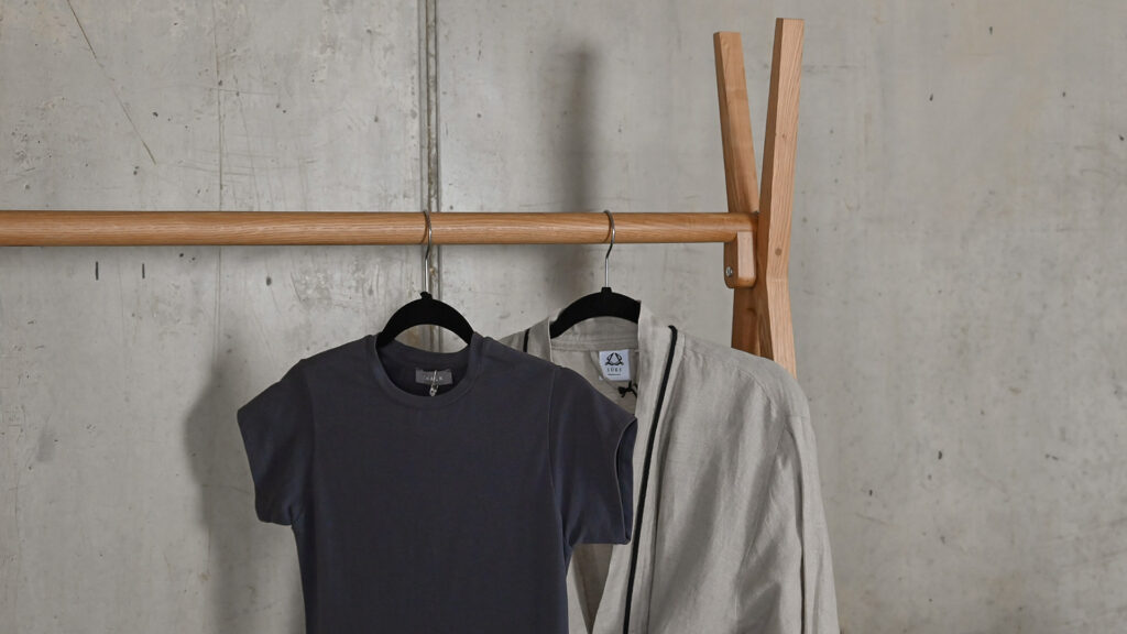 Closeup image of the rail section of the Solid Oak Clothes Rail, with a grey t-shirt and cotton robe hanging from it.