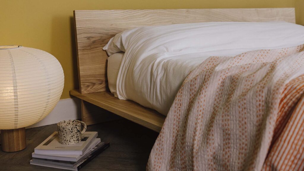closeup of a reversible bedspread on white bed linen. One side thick orange and white stripes, the other orange stitches. Bedspread folded over so that both sides are visible.