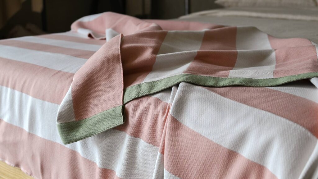 Pink and white striped throw with green border laid across a bed.