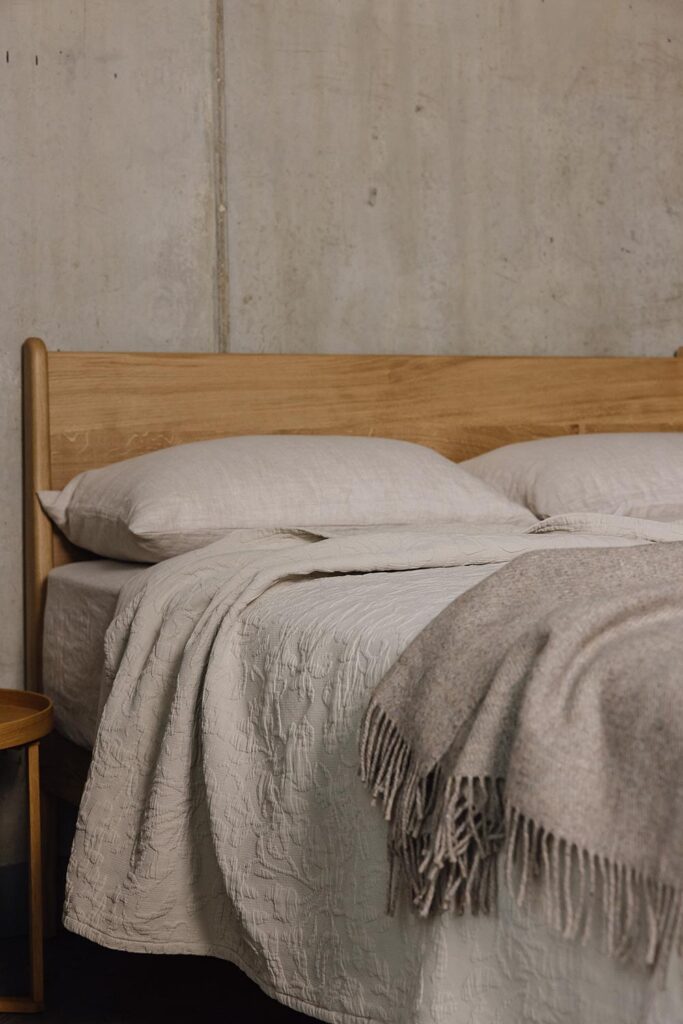 Portrait shot of an oak bed with beige linen and a griege woollen throw.