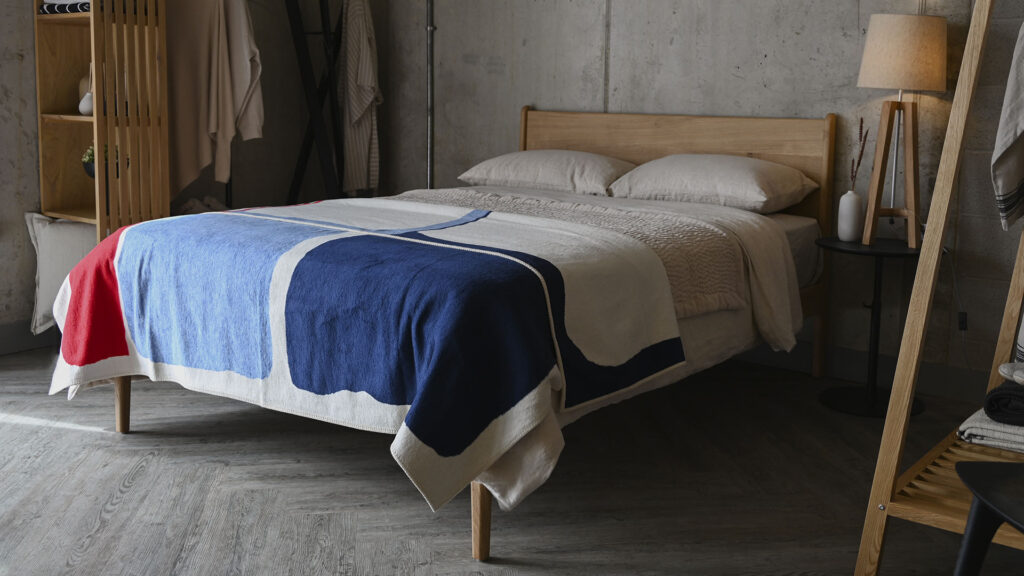 Oak bed frame in bedroom scene, with stone linen and a blue and red modern abstract throw on the top.