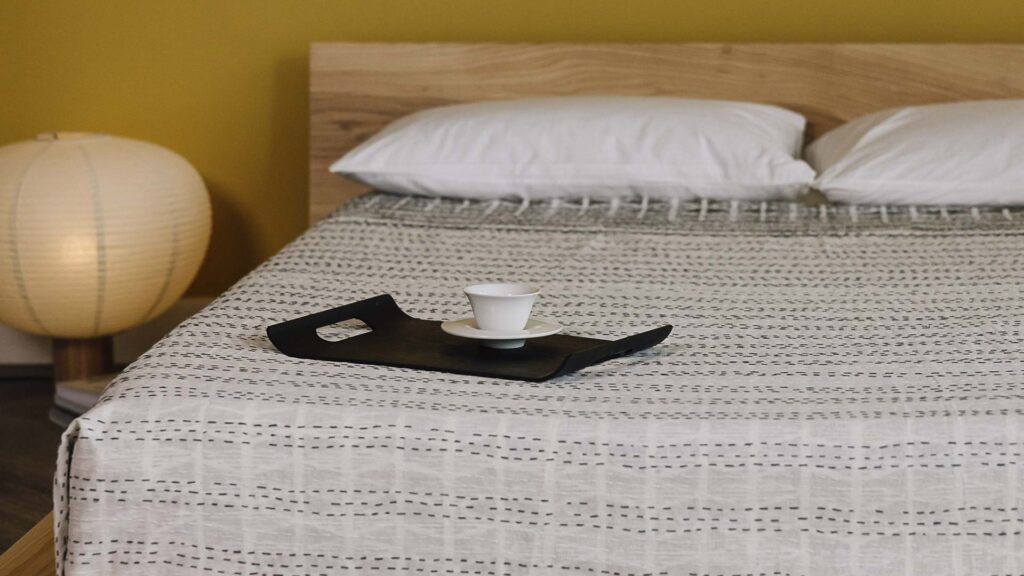 close up of black tray and mug sitting on top of a striped bedspread.