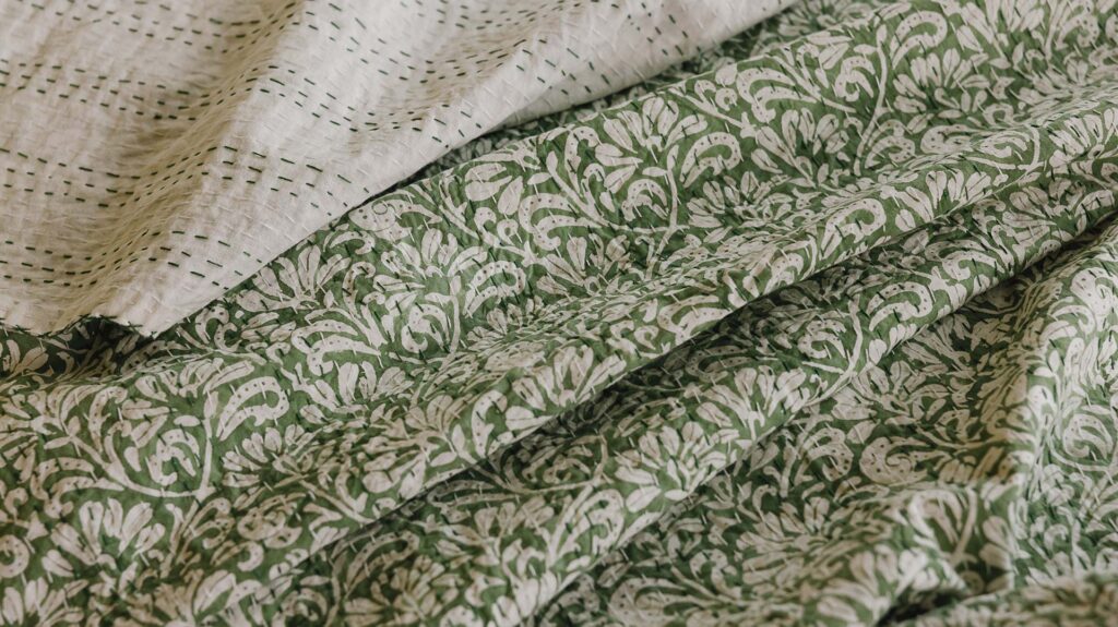 Close up of green floral patterned kantha bedspread, top folded down to show the green stitching pattern on the reverse.