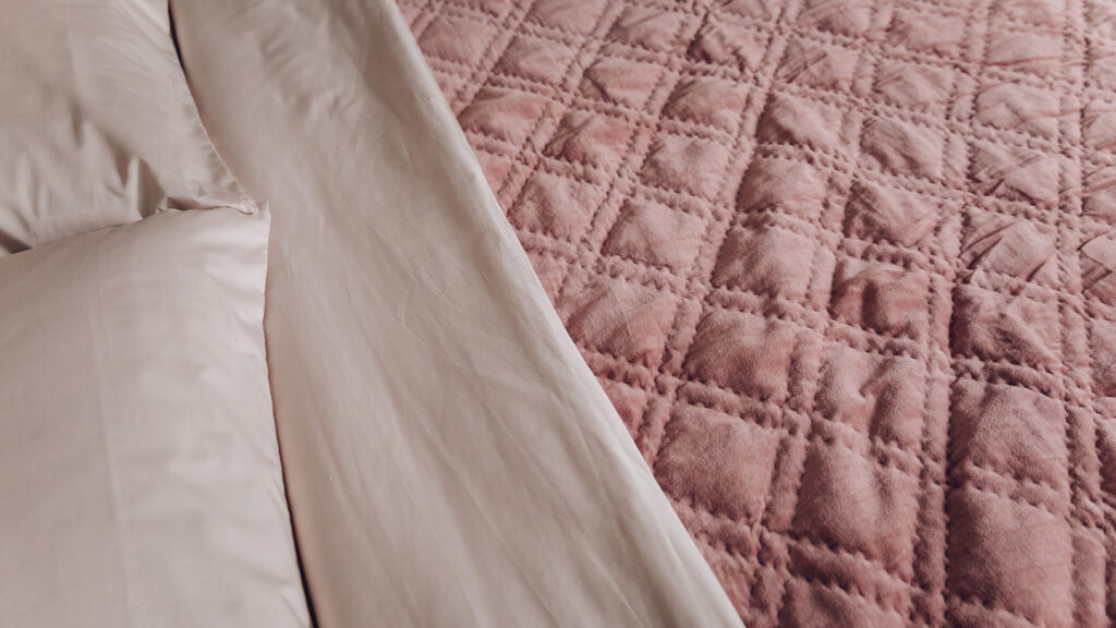 dusky rose coloured quilted velvet bedspread shown with shell pink bedding