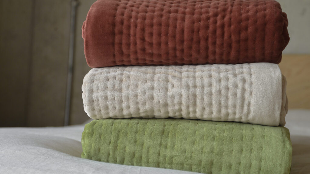 stack of three velvet quilts - wine red, almond and olive green.
