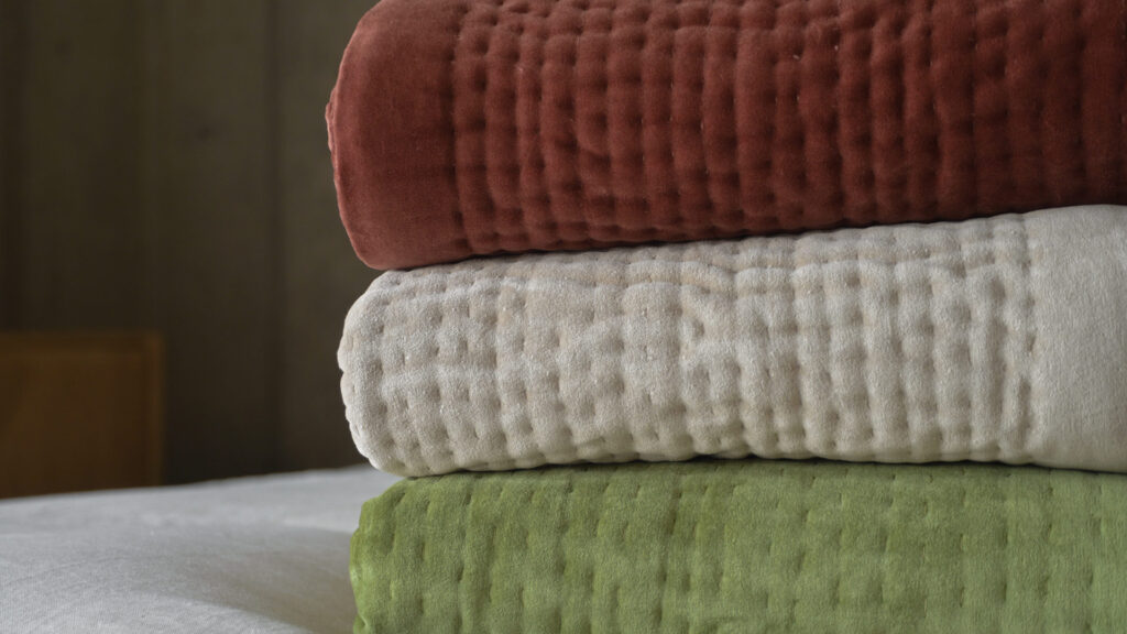 stack of three velvet quilts - wine red, almond and olive green.