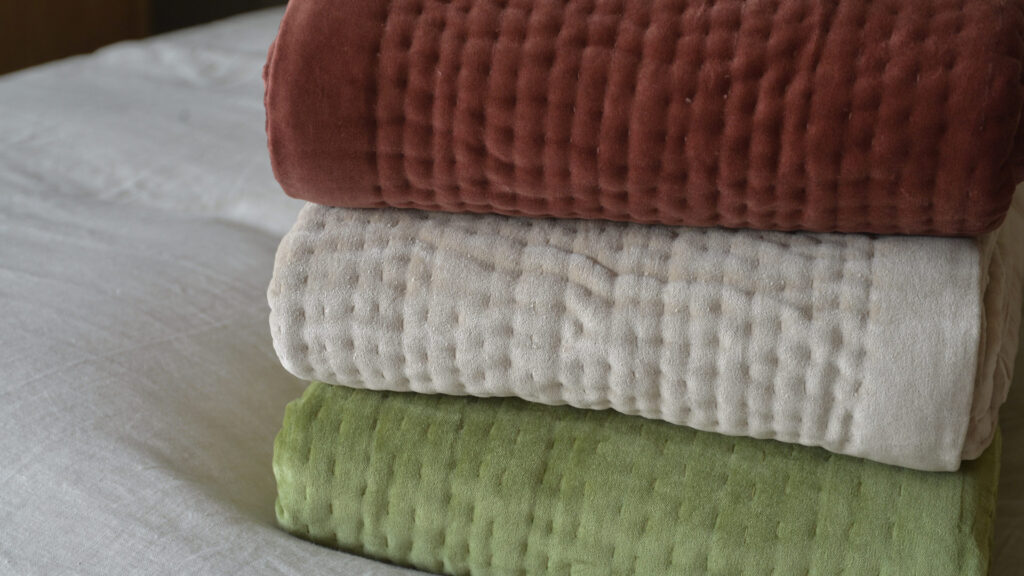 stack of three velvet quilts - wine red, almond and olive green.