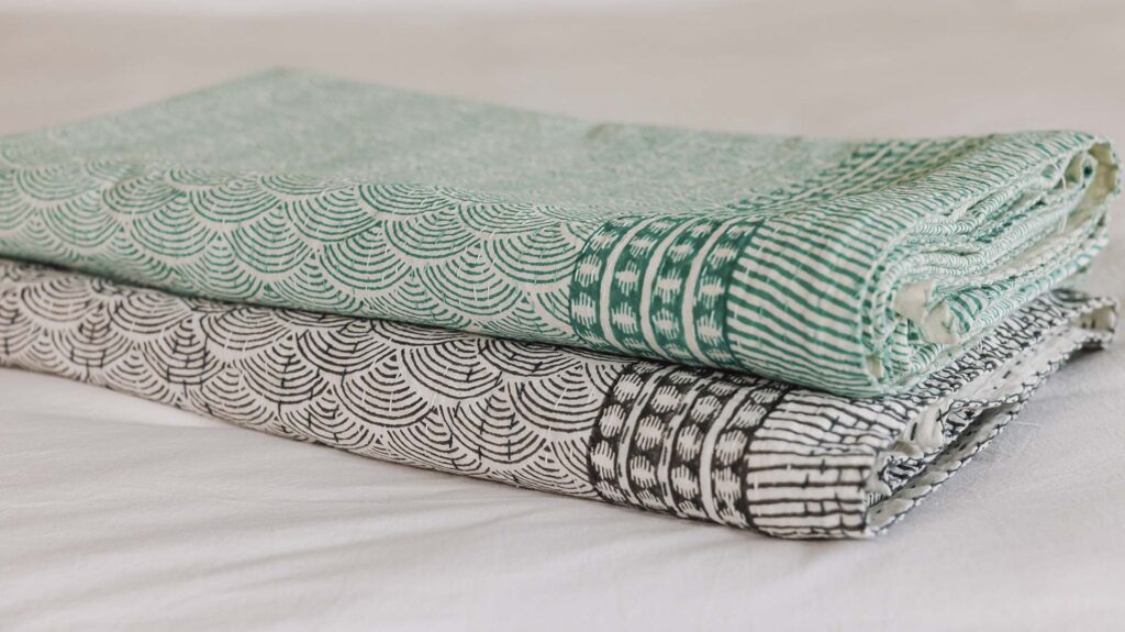 2 Kantha Style bedspreads neatly folded and stacked. Bottom one with a grey block print, top green.