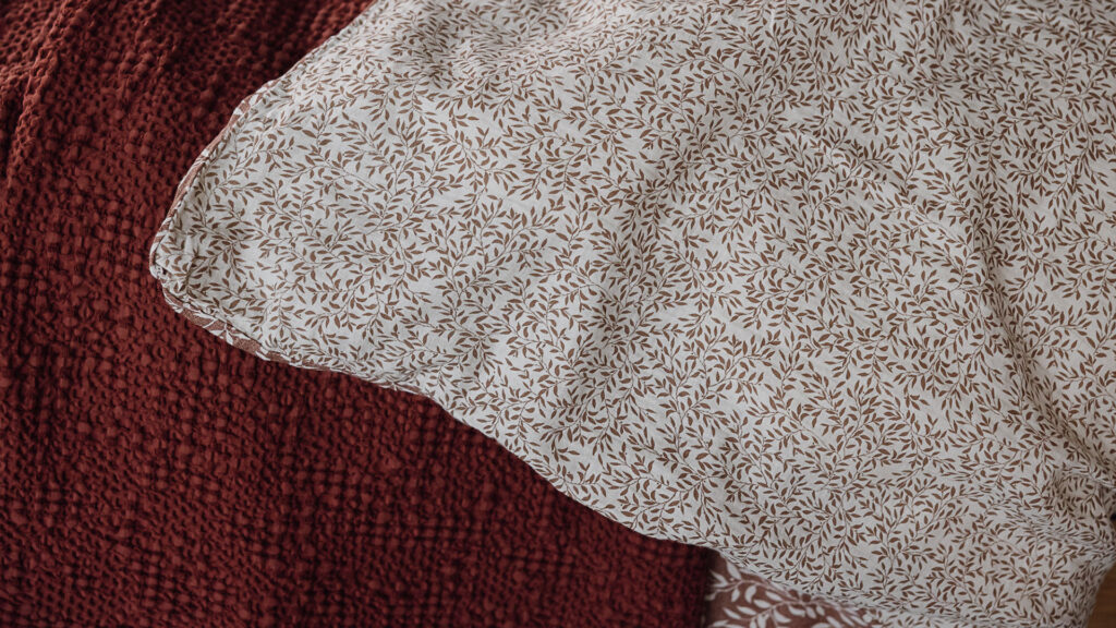 close up of reverse of duvet, white background with rust red mini leaf print.
