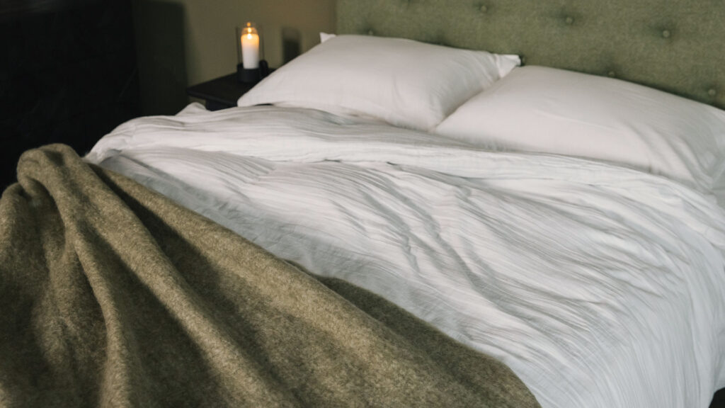 olive green chunky wool throw shown with white muslin like cotton bedding